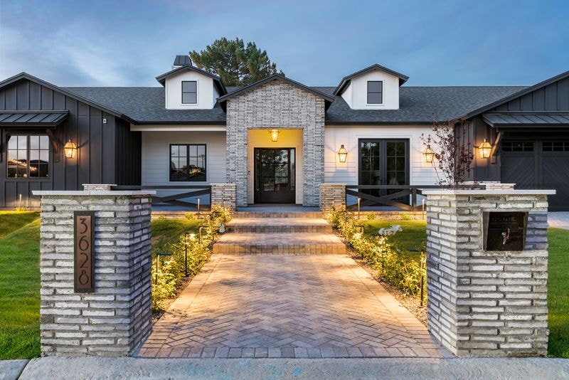 Luxury home exterior with illuminated brick pathway and landscape lighting at dusk