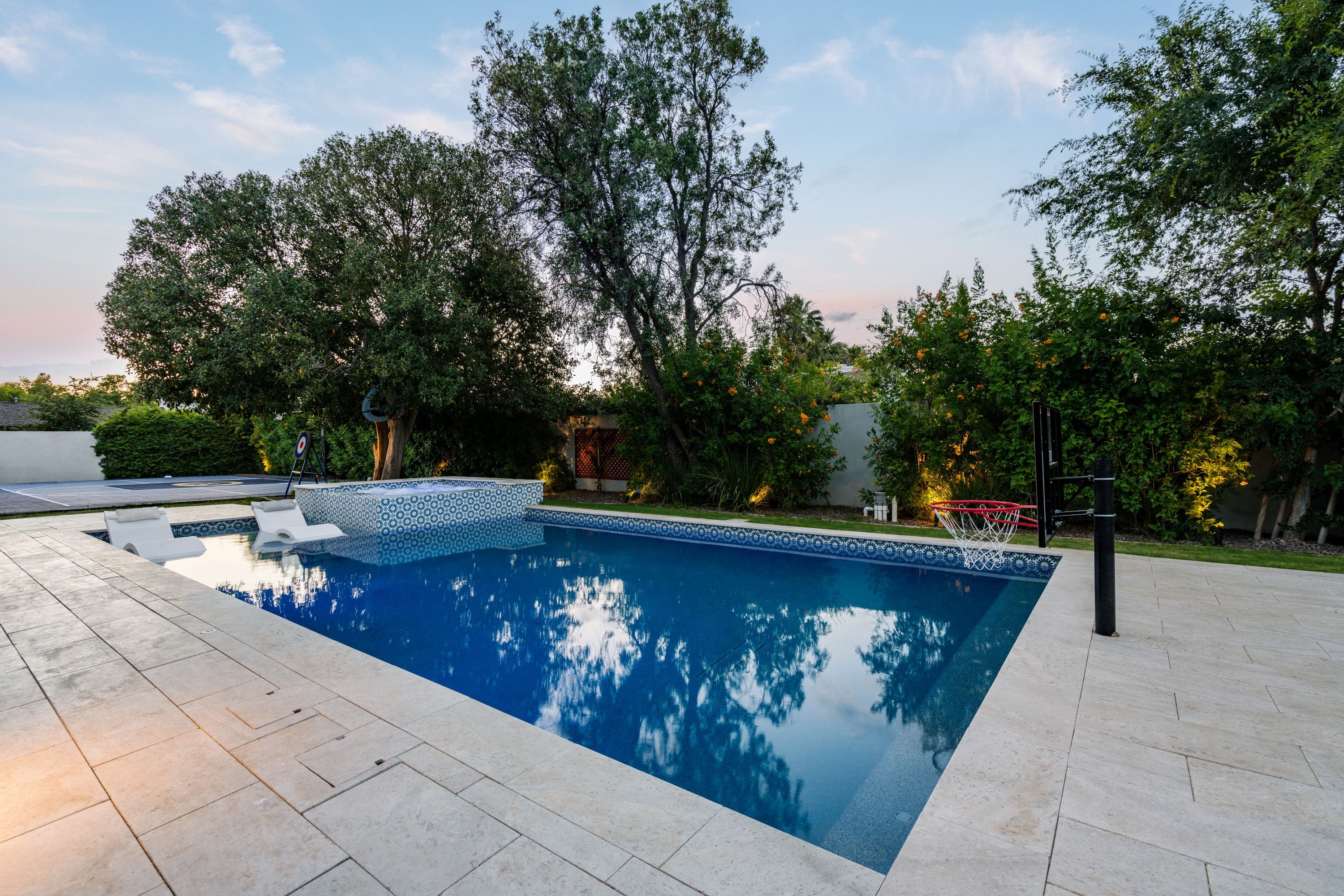 Luxury pool with blue geometric tile spa, Baja shelf, and travertine coping at dusk