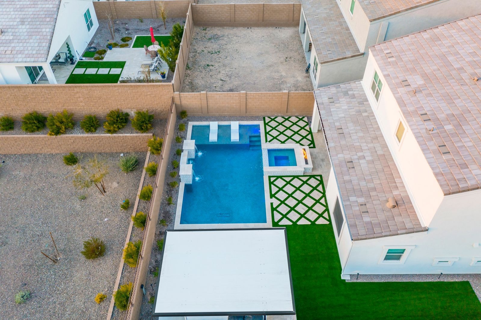 Aerial view of pool and spa with diamond lattice turf pattern and travertine deck
